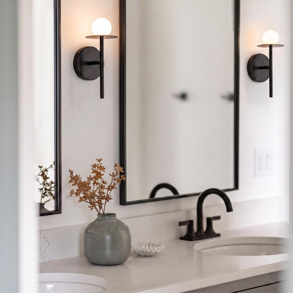 A modern bathroom with two Sol LED Wall Sconces in matte black featuring frosted globe shades flanking a black-framed mirror over a white marble countertop.