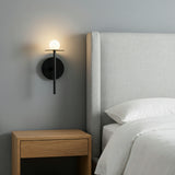 Matte Black globe wall sconce in a Modern Bedroom with a light grey upholstered headboard.