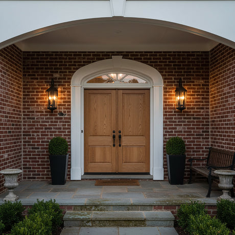 Asbury Outdoor Wall Light, Medium 29" Black - Two black lantern-style sconces illuminate a brick facade flanking a double wooden door with a white arched entryway.