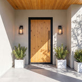 Two Alden Small Wall Lights in Black next to a wooden front door with black frame under a porch on a sunny day