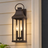 A traditional home entry features the glowing Ainsley Outdoor Wall Light, Medium 21" Oiled Bronze mounted on cream siding beside a dark door at dusk.
