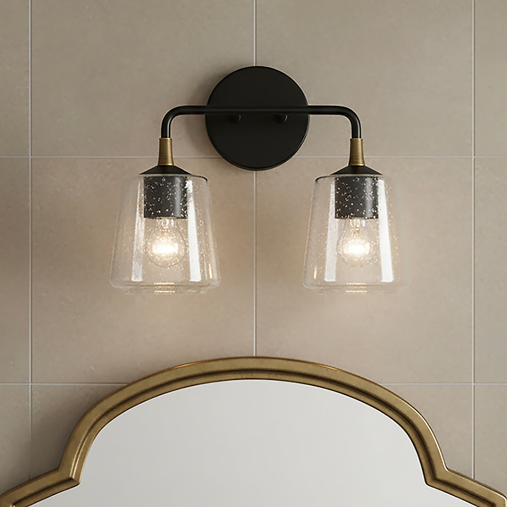 Malin 2 Light Vanity - Two lights with seeded glass shades and brass accents on a matte black fixture against a tiled wall, above a decorative mirror.