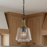 A transitional kitchen features the Malin Pendant 9", Matte Black with Brass Accents with seeded glass hanging over a counter against a backdrop of natural wood cabinetry.