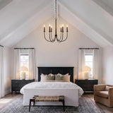 A modern farmhouse bedroom featuring the Malin 6 Light Chandelier in matte black with brass accents suspended from a vaulted beamed ceiling over a white upholstered bed.