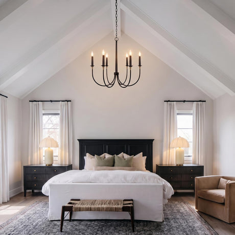 A modern farmhouse bedroom featuring the Malin 6 Light Chandelier in matte black with brass accents suspended from a vaulted beamed ceiling over a white upholstered bed.