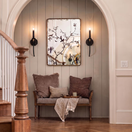 A transitional foyer alcove features two Malin Wall Sconces in Matte Black with Brass Accents flanking a botanical mirror above a cushioned wooden bench.