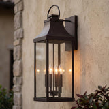 A Mediterranean home exterior featuring the Ainsley Outdoor Wall Light, Extra Large 27" Oiled Bronze lantern glowing at dusk on a stucco wall beside a stone corner.