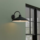 Black wall-mounted outdoor light fixture on a green wall with a window in the background.