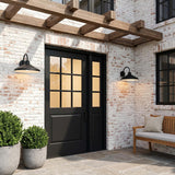 A modern farmhouse patio with two matte black Eton Outdoor Wall Light, Large 17" Black barn lights flanking a door on white-washed brick at dusk under a pergola.