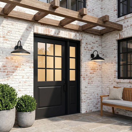 A modern farmhouse patio with two matte black Eton Outdoor Wall Light, Large 17" Black barn lights flanking a door on white-washed brick at dusk under a pergola.