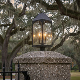 Chester Outdoor Post Light, Black - A black post light fixture is displayed atop a stone column with Spanish moss-draped trees in the background.