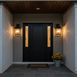 Beckett Outdoor Wall Light, Large 24" Black - Two black lanterns with clear glass panels flanking a black front door, illuminated warmly.