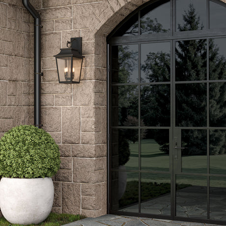 Beckett Outdoor Wall Light, Large 24" tall in Oiled Bronze finish on a stone wall with a large glass door and potted plant.