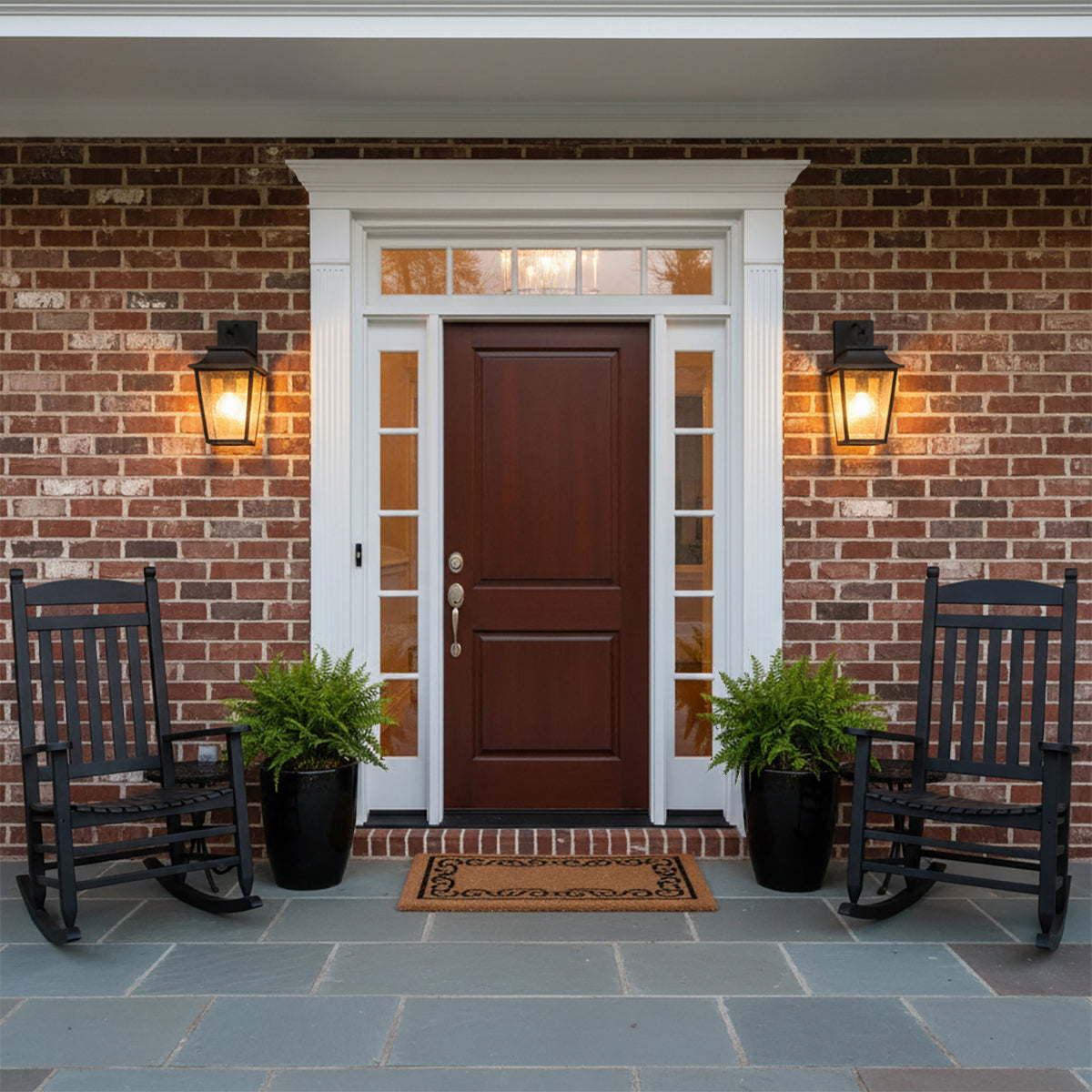 Beckett Outdoor Wall Light, Small 16" Black - Two black outdoor wall lights flanking a dark wood front door, with black rocking chairs and potted ferns on a slate patio.
