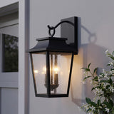 A transitional exterior wall with the matte black Beckett Outdoor Wall Light glowing at dusk beside a white trimmed door and climbing white jasmine flowers.