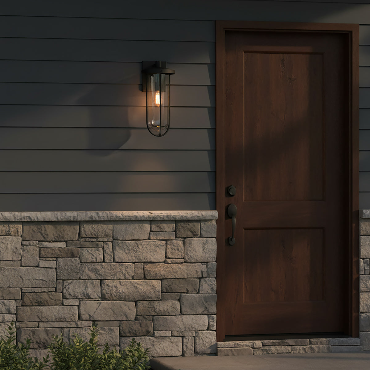 Orson Outdoor Wall Light, Medium 18" Black - A black outdoor wall light illuminates the exterior of a house next to a dark wooden door and stone siding.