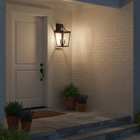 Ellery Outdoor Wall Light, Medium 19" Black - A black lantern-style outdoor wall light is mounted on a white brick wall next to a white door with plants on the porch.