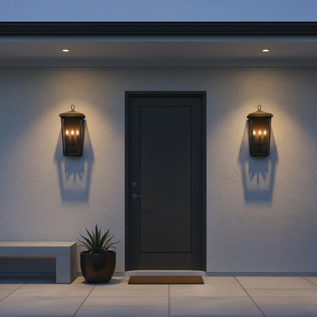 Leighton Outdoor Wall Light, Large 24" Black - Two black lanterns with glowing bulbs flank a dark grey door on a textured white wall, with a modern bench and potted plant to the left.