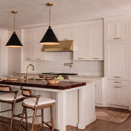 A modern farmhouse kitchen with two matte black and aged brass cone pendants hanging over a walnut butcher-block island featuring white shaker cabinets and subway tile.