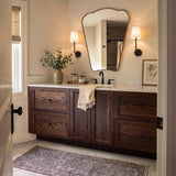 A transitional bathroom with two matte black Elowen Wall Sconces featuring linen shades flanking an organic-shaped mirror over a dark wood vanity and quartz countertop.