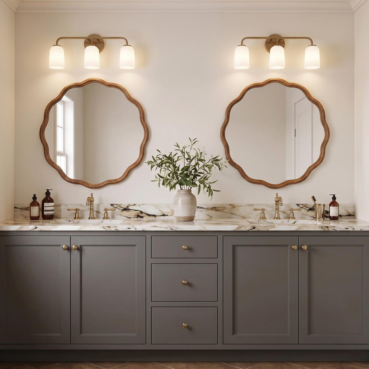 A transitional bathroom with two aged brass and frosted glass vanity lights over scalloped wood mirrors, a white marble countertop, and gray shaker cabinets.