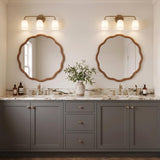 A transitional bathroom with two aged brass and frosted glass vanity lights over scalloped wood mirrors, a white marble countertop, and gray shaker cabinets.