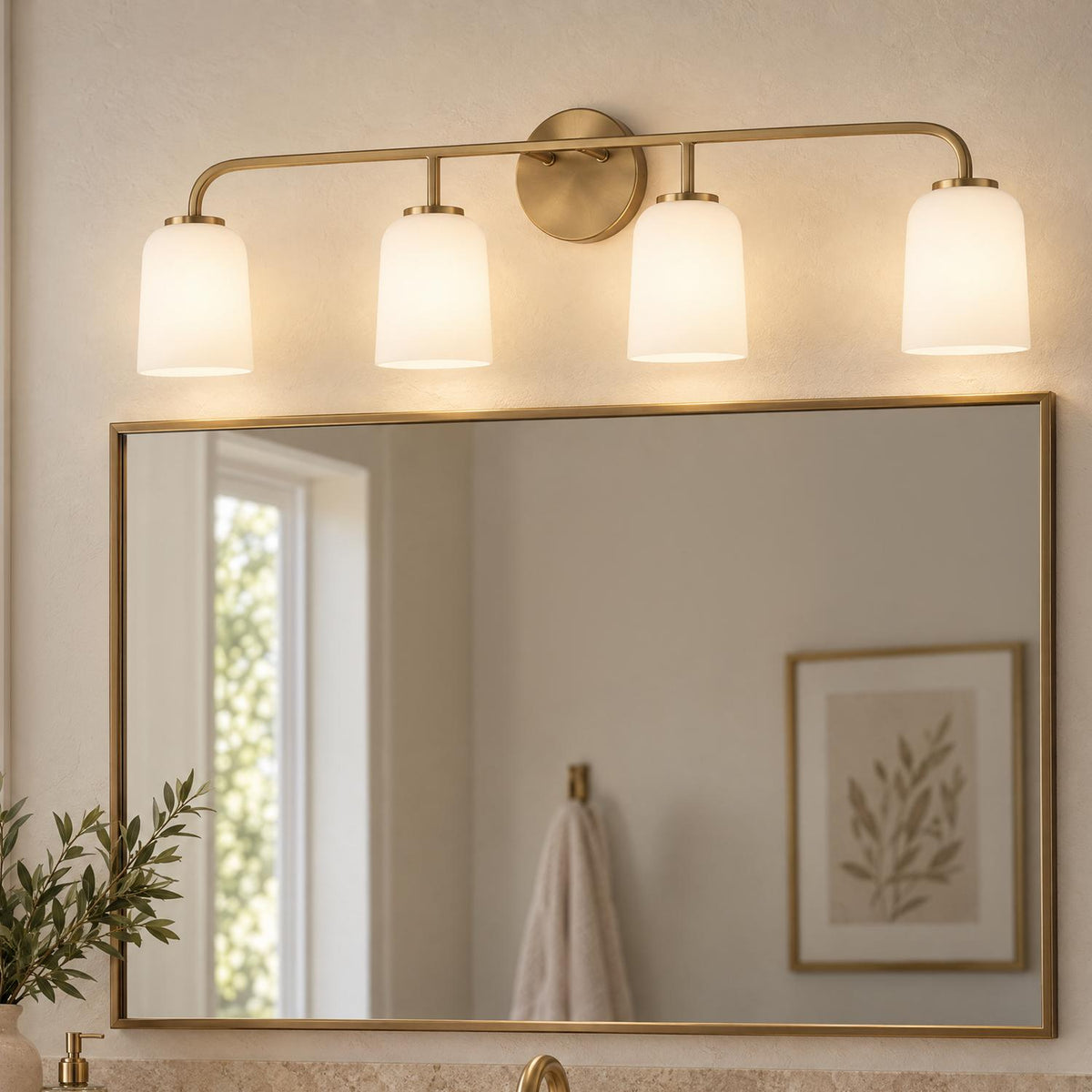 A transitional bathroom features the Elira 4 Light Vanity, Aged Brass with frosted glass shades mounted above a thin brass-framed rectangular mirror.