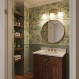 A traditional bathroom featuring the Harper 3 Light Vanity, Aged Brass with white shades above a round mirror, green botanical wallpaper, and a walnut vanity cabinet.