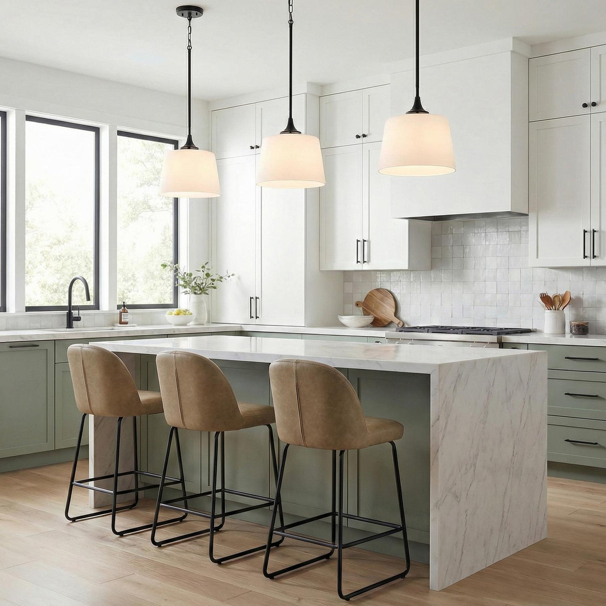A transitional kitchen features three matte black pendants with white linen shades hanging over a white marble waterfall island and sage green lower cabinets.
