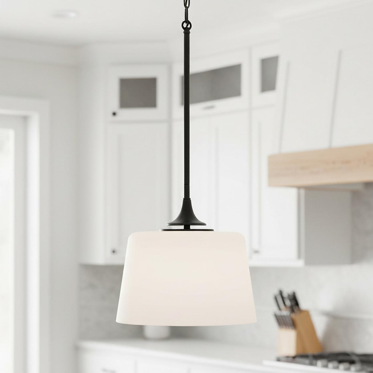 A transitional kitchen features a Harper Pendant 12", Matte Black with white glass hanging along the perimeter near white shaker cabinets and a wood trimmed range hood.