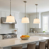 A transitional kitchen features three Harper Pendant 12", Brushed Nickel fixtures with white glass shades hanging over a white quartz island and white shaker cabinets.