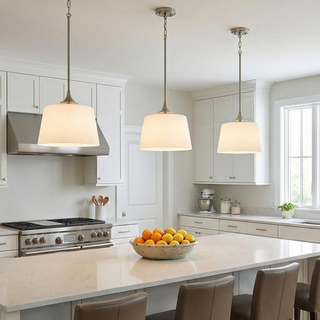 A transitional kitchen features three Harper Pendant 12", Brushed Nickel fixtures with white glass shades hanging over a white quartz island and white shaker cabinets.