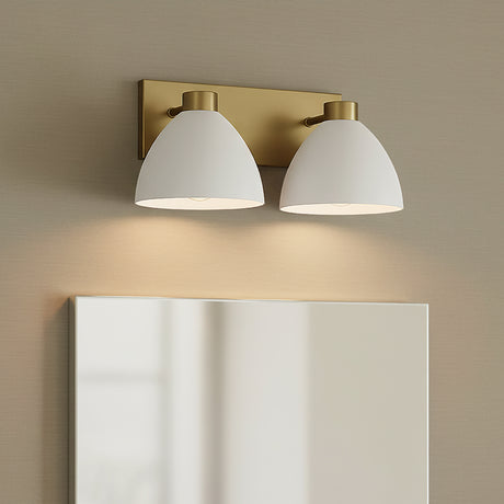 Cleo 2 Light Vanity, white and Aged Brass - Two white dome-shaped vanity lights with aged brass accents mounted above a clean, white rectangular mirror against a textured beige wall.
