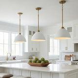 A transitional white kitchen features three Cleo Pendant 13 inch White and Aged Brass fixtures over a large white island with shaker cabinets.