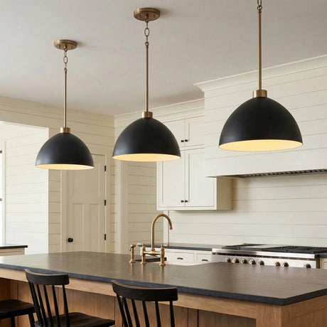 A farmhouse kitchen features three Cleo Pendant 13" Matte Black and Aged Brass fixtures over the dark stone island and wood cabinetry against white shiplap walls.