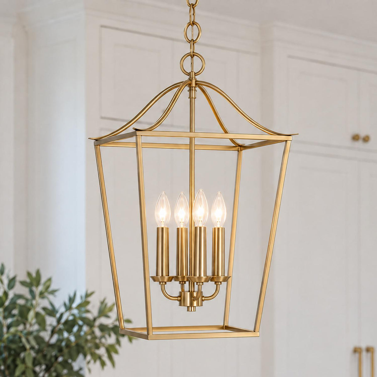 A transitional kitchen features the Eloise Lantern Pendant 16", Matte Brass suspended in front of white paneled cabinetry with brass hardware and greenery.