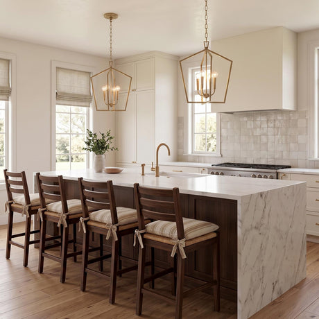 A transitional kitchen with two Clara Lantern Pendant 17", Aged Brass fixtures over a white marble waterfall island, featuring dark wood stools and a tile backsplash.