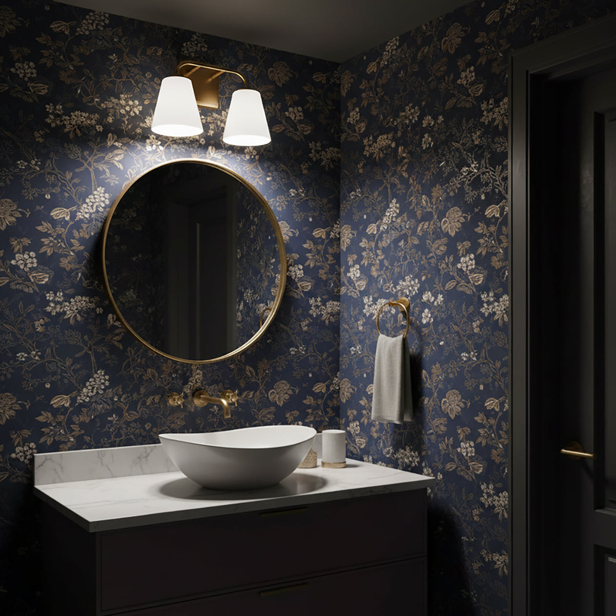 Dark bathroom with navy and tan floral wallpaper, a round mirror, and the Brier 2 Light Vanity Light above, in Aged Brass