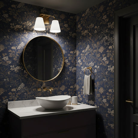 Dark bathroom with navy and tan floral wallpaper, a round mirror, and the Brier 2 Light Vanity Light above, in Aged Brass