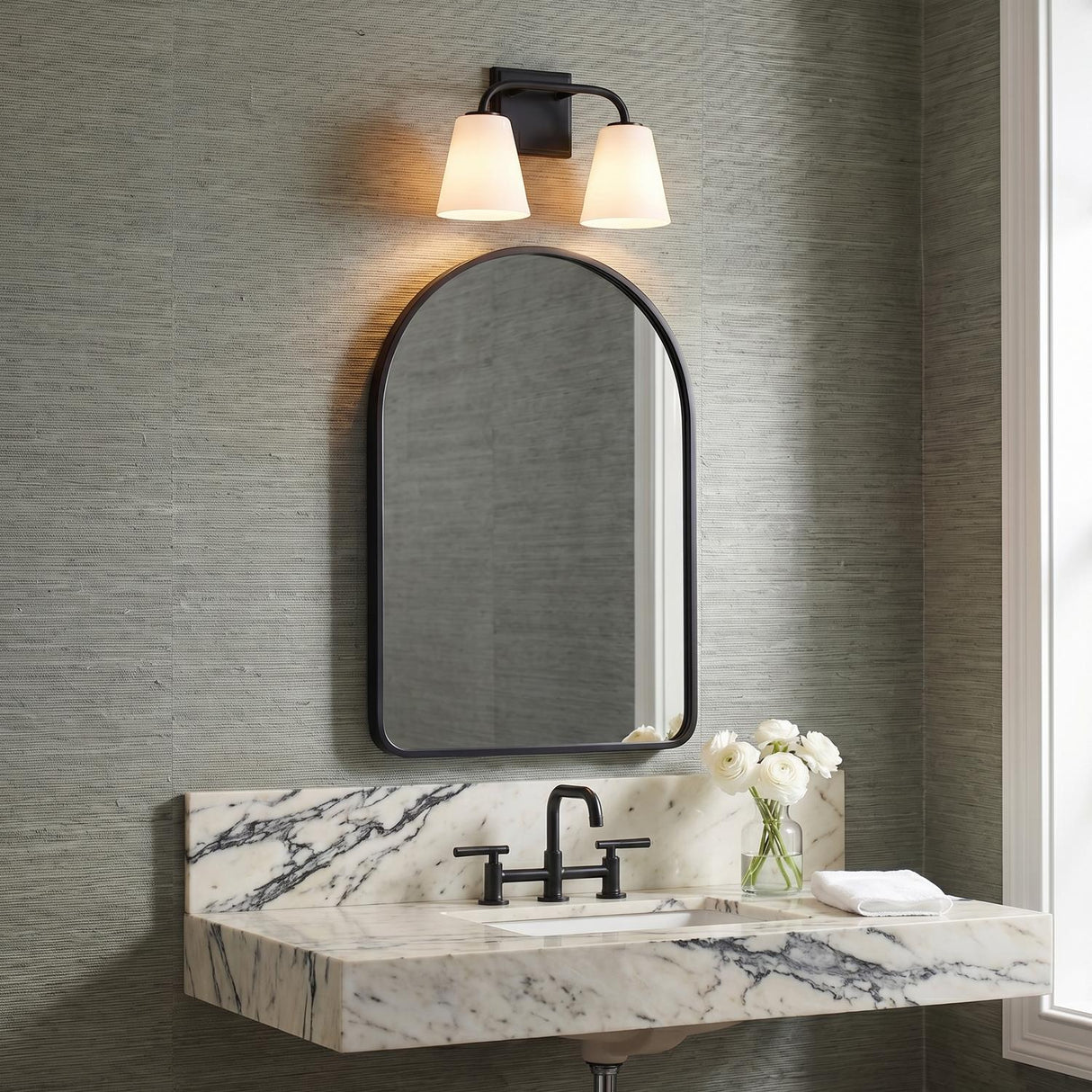 A contemporary bathroom featuring the Brier 2 Light Vanity, Matte Black with frosted glass shades installed above a black arched mirror and a veined marble floating counter.