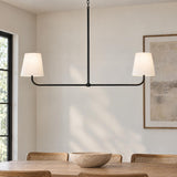 A transitional dining room with a matte black linear pendant featuring off-white linen shades hanging over a natural wood dining table and cane back chairs.