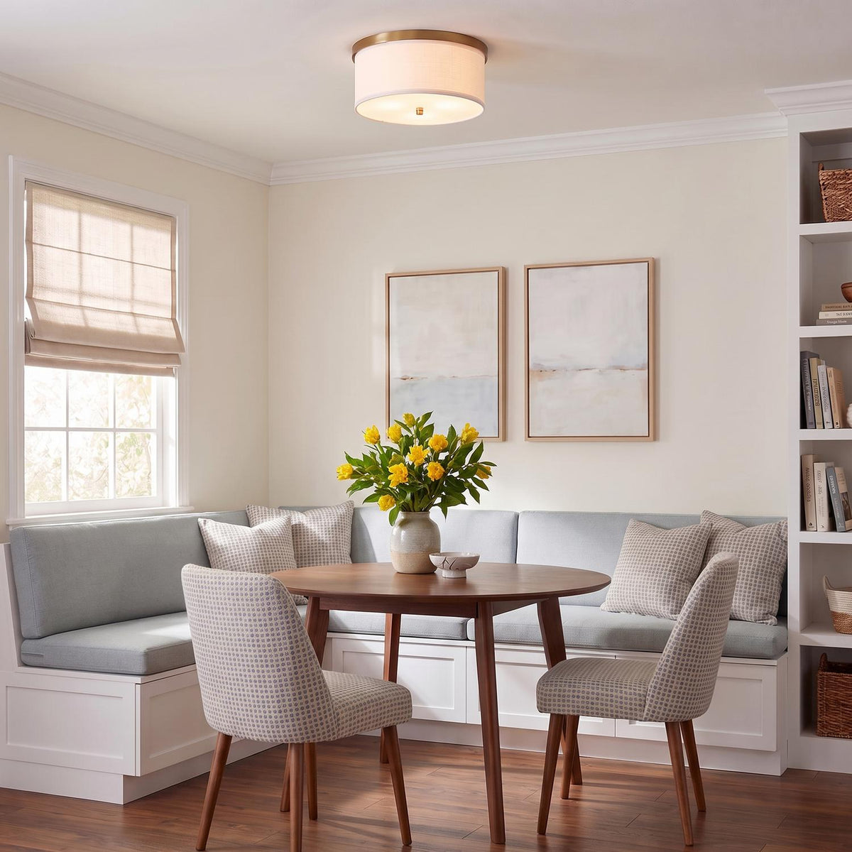 A transitional dining room with the Wells Flush Mount 16", Aged Brass with a white linen shade mounted over a round wood table and light blue banquette.