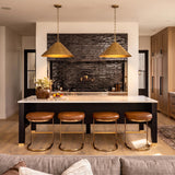 A modern farmhouse kitchen with two aged brass cone pendants over a black island with a white quartz countertop and a textured black backsplash.