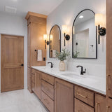 A transitional bathroom with four Whitby Wall Sconces in glossy black and aged brass with linen shades flanking two arched mirrors over a white quartz double vanity.