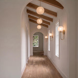 A transitional foyer with the Tova Pendant 14", Matte Brass with Cloud Opal Glass suspended from wood beams above a hallway with light wood flooring.