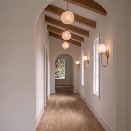 A transitional foyer with the Tova Pendant 14", Matte Brass with Cloud Opal Glass suspended from wood beams above a hallway with light wood flooring.