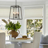 A transitional dining nook with the Tilden Lantern Pendant 21", Textured Black hanging over a white pedestal table with a large rattan vase and greenery.