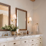 A transitional bathroom with two Dorian Wall Sconce 14", Matte Brass fixtures with linen shades flanking wood-framed mirrors above a white marble double vanity.