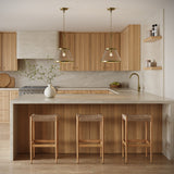 Two Elora 15" wide Pendants, in Aged Brass with Hammered Glass, hung above a kitchen peninsula with natural stone countertops and wood cabinets.