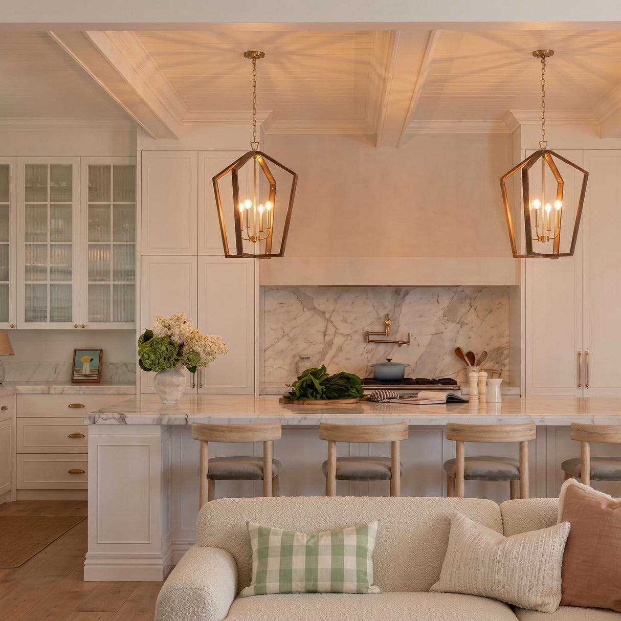 A transitional kitchen with two Talin Lantern Pendants in chestnut and matte brass hanging over a white marble island under a coffered beamed ceiling.